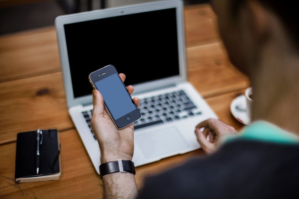 person on computer and looking at phone